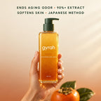 Gyrah Persimmon Body Wash held up in warm sunlight with a fresh persimmon.